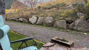 A garden with a stone wall, a chair, and a view of a hillside.