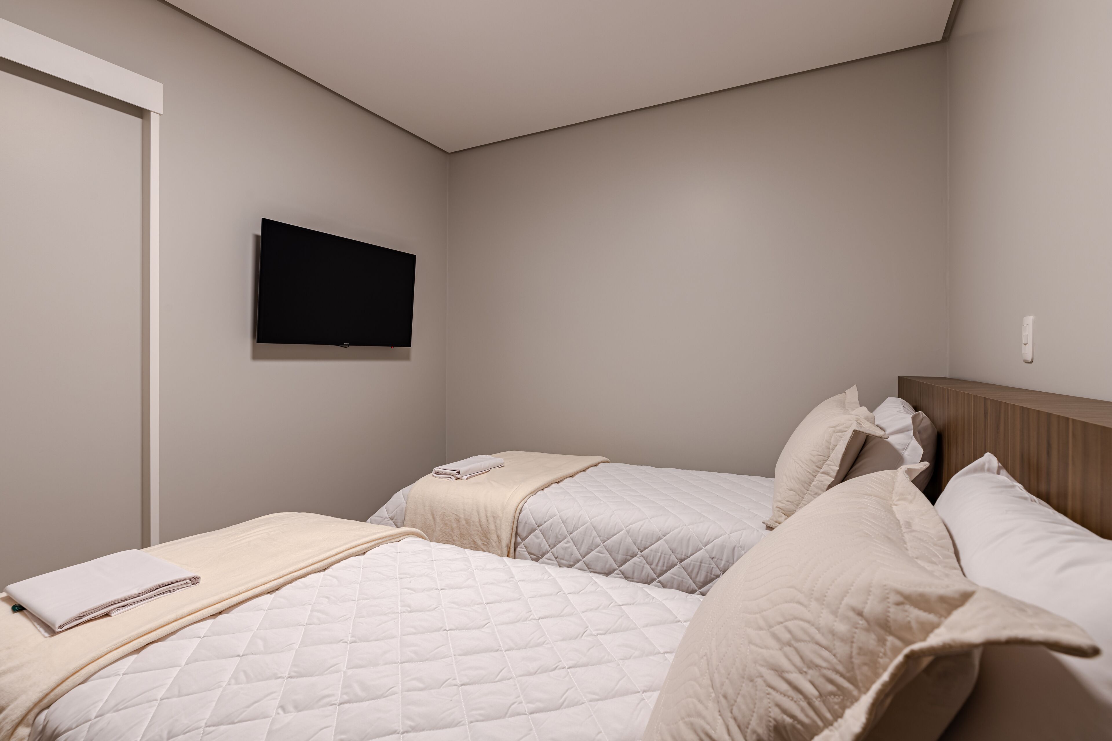 Un dormitorio con dos camas, un televisor de pantalla plana montado en la pared y una puerta.