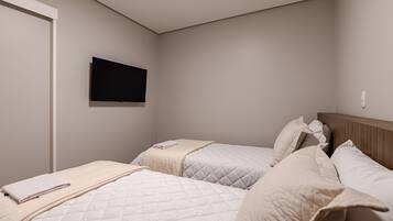 Un dormitorio con dos camas, un televisor de pantalla plana montado en la pared y una puerta.
