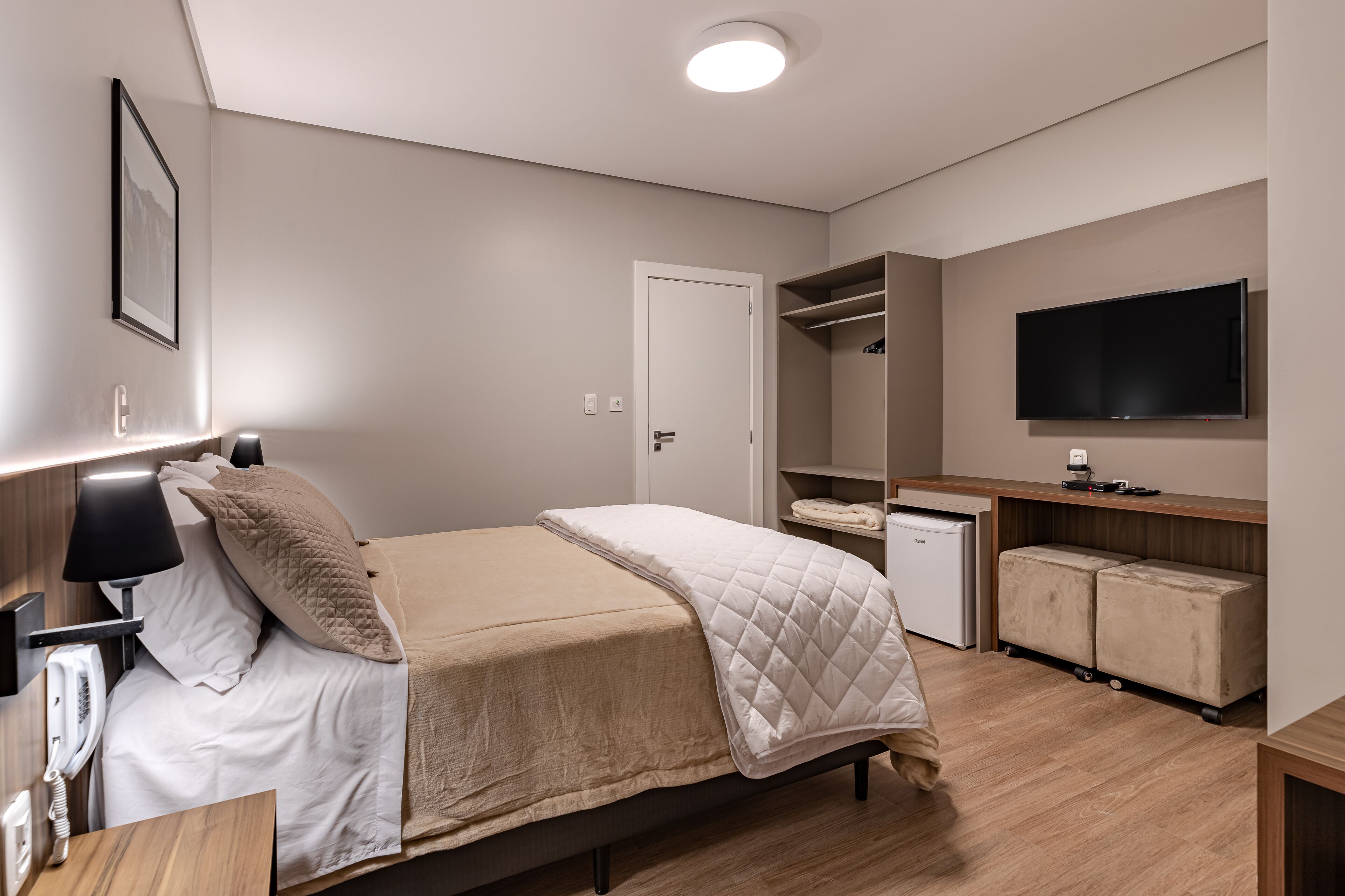 A modern bedroom with a bed, bedside table, lamp, and a TV mounted on the wall.
