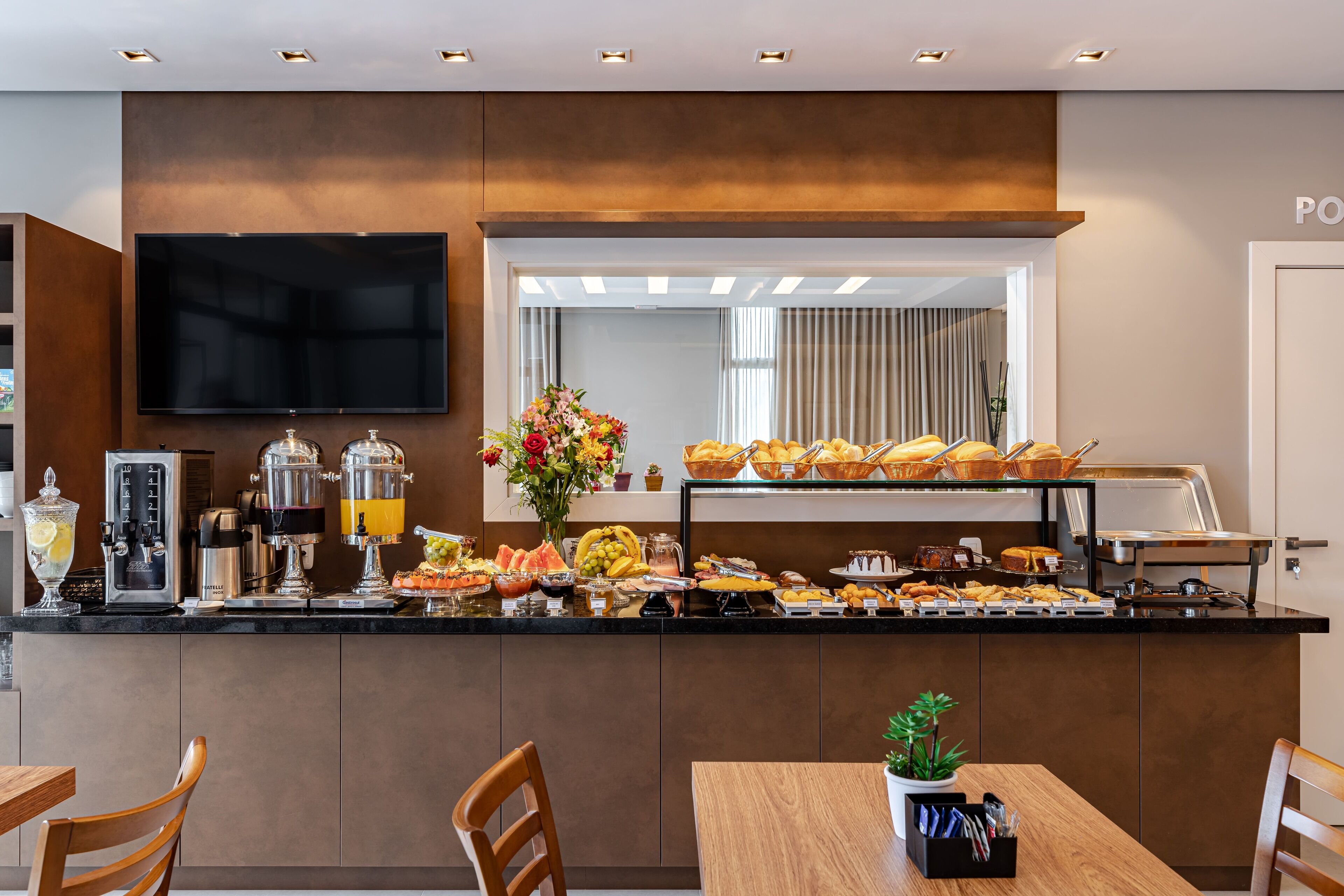 A breakfast bar with a variety of food items, a coffee machine, and a television mounted on the wall.
