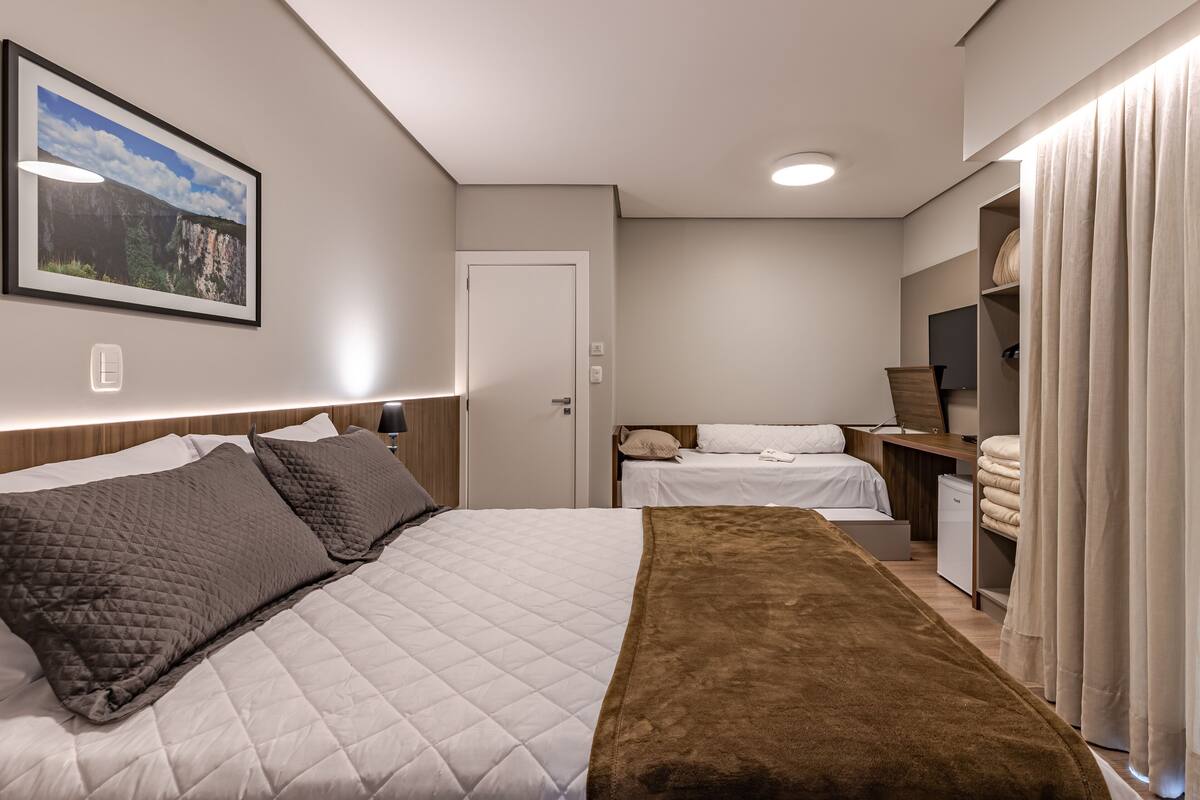 Un dormitorio con cama, mesitas de noche, armario, escritorio y televisor.