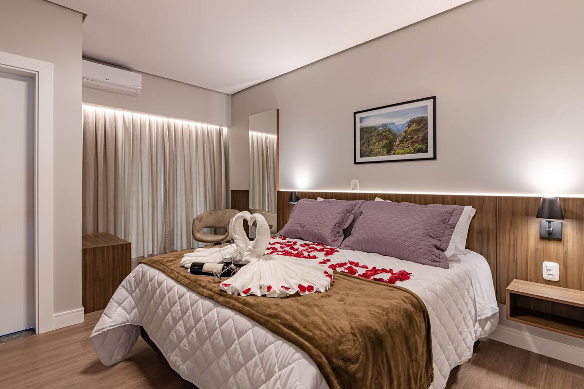 Habitación de hotel con cama, cabecero, mesita de noche, lámpara de pared e imagen enmarcada en la pared.