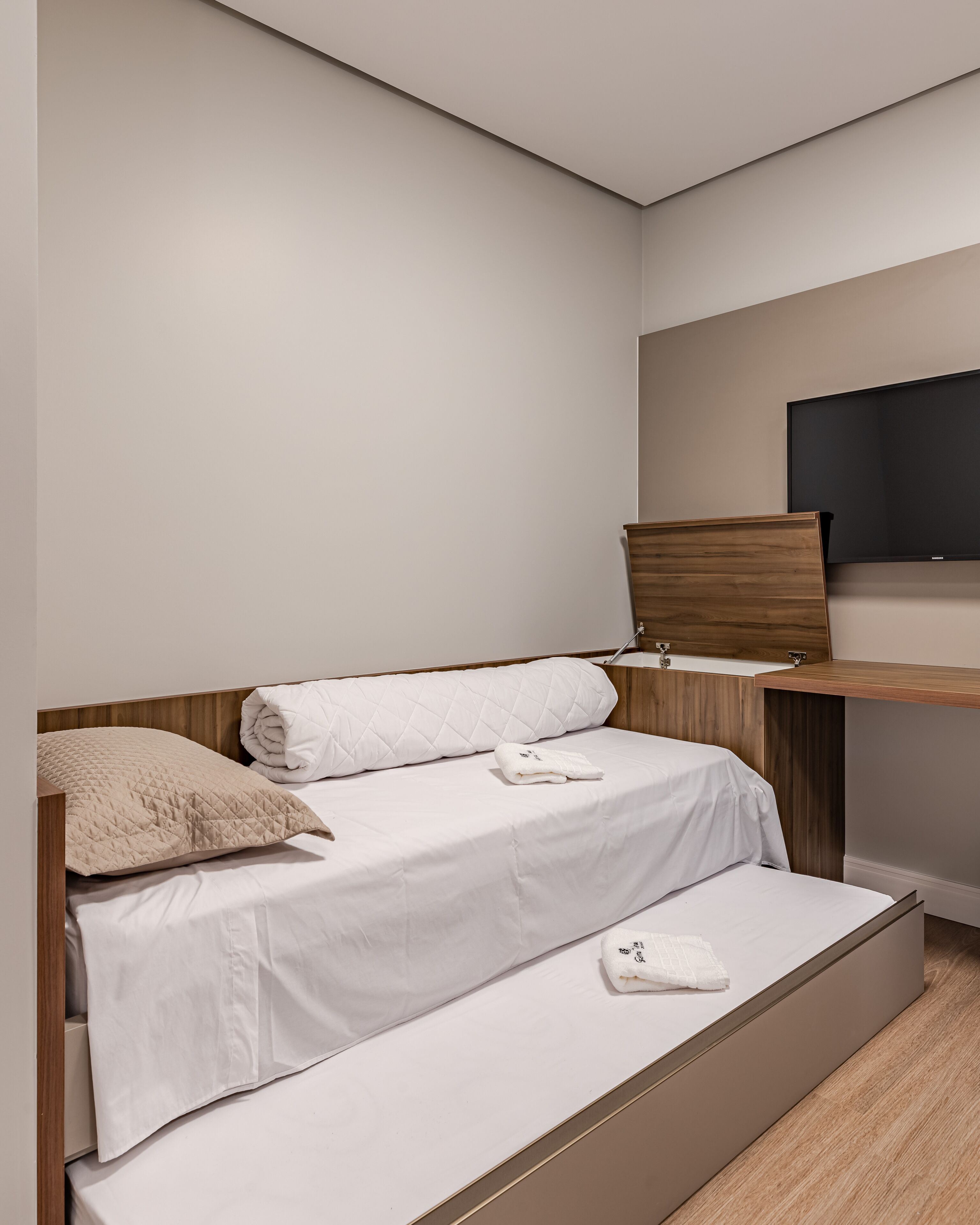 A modern bedroom with a bed, a wooden nightstand, a TV mounted on the wall, and a built-in bench.