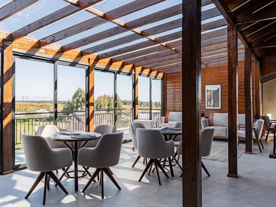 Un amplio espacio exterior con vigas de madera y ventanas grandes, que incluye una mesa y sillas de comedor, un sofá y una chimenea.