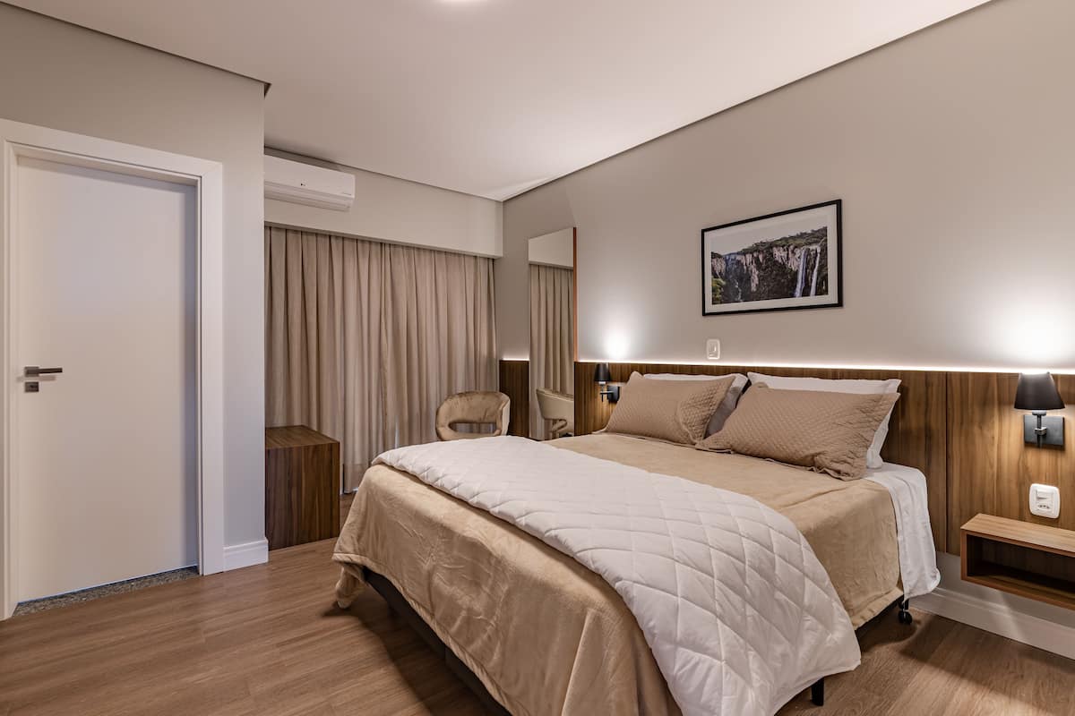 Un dormitorio moderno de hotel con una cama grande, una mesita de noche, una silla y una lámpara de pared.