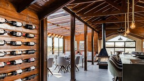A spacious room with a wooden wall displaying numerous wine bottles, a bar area with stools, and a view of the outdoors through large windows. - Pousada Serra Verde (Cambara do Sul)
