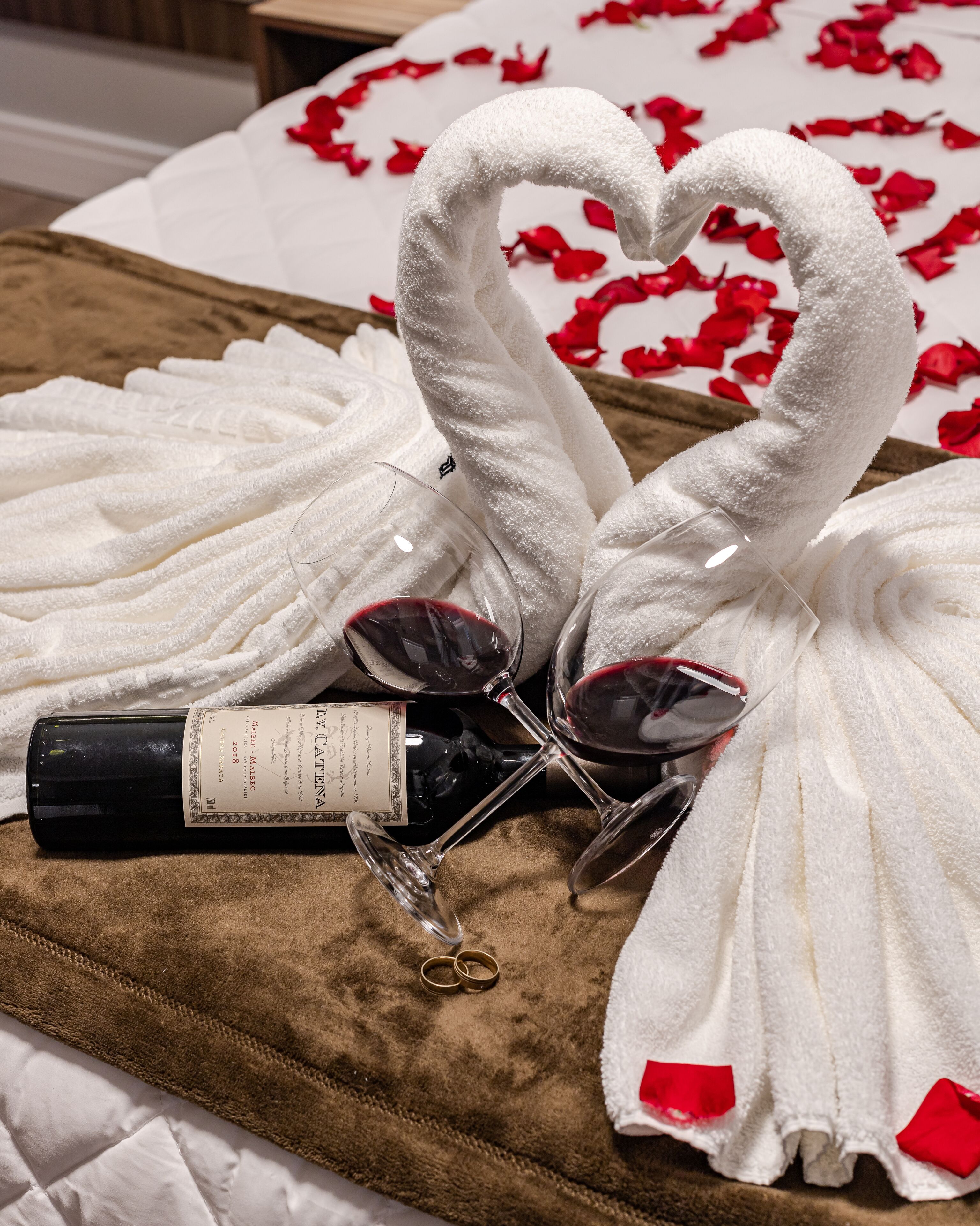 A bed with a brown blanket, white towels, and a bottle of wine.