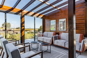 Una cabaña de madera moderna con balcón de cristal, amoblada con un sofá y dos mesitas.