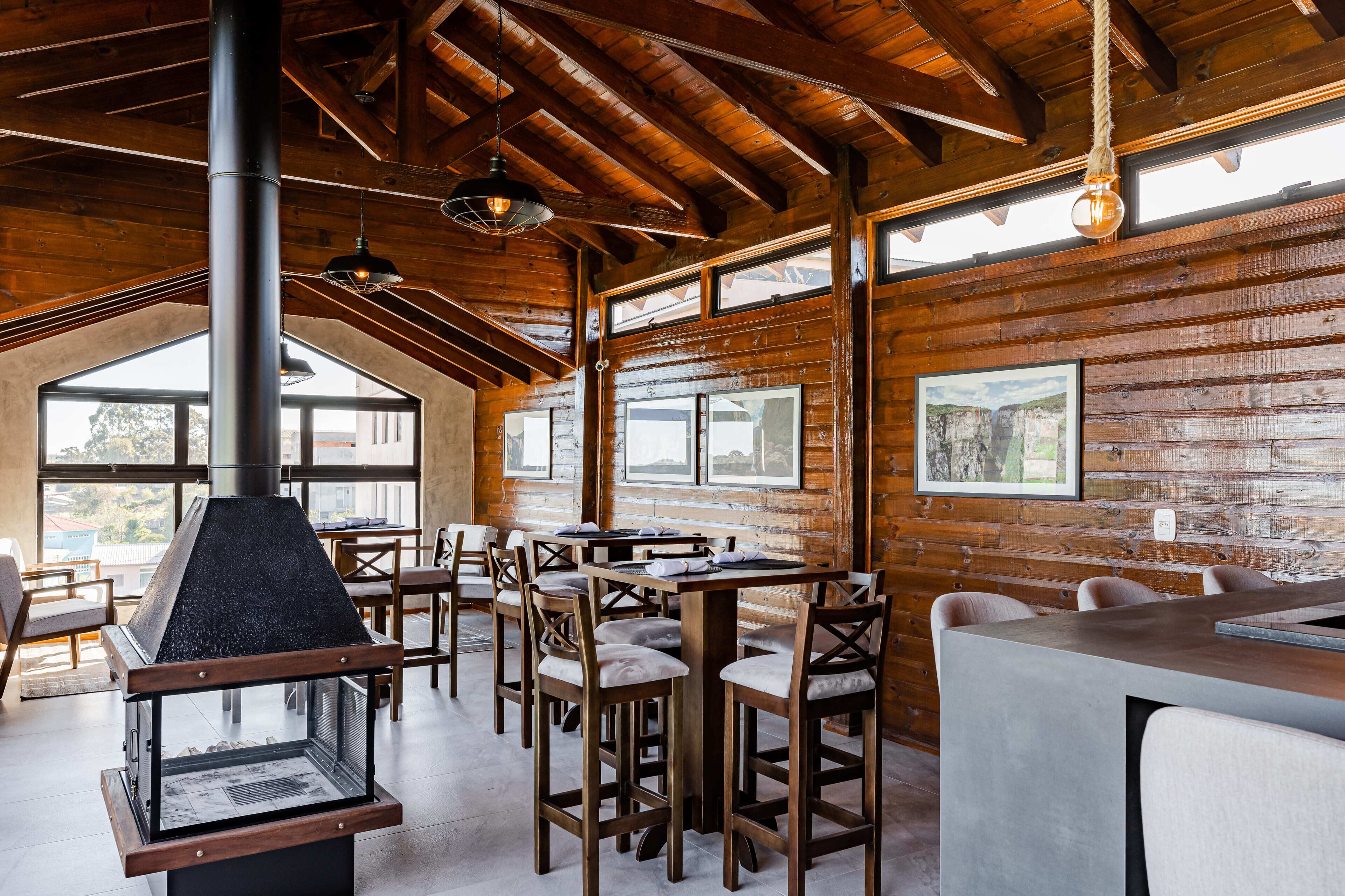 Un intérieur rustique en bois, avec un poêle à bois central, des tables et des chaises disposées pour les repas.