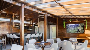 A modern bar area with wooden beams, white bar stools, and a television mounted on the wall. - Pousada Serra Verde (Cambara do Sul)
