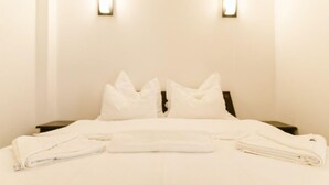 Una habitación de hotel con una cama bien hecha, dos mesitas de noche y dos lámparas fijadas a la pared.