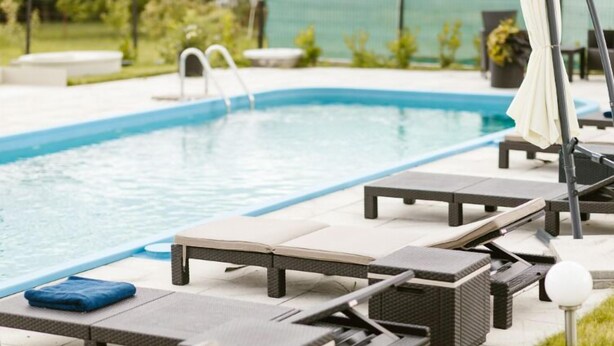 Un área de piscina con sillones de descanso y una sombrilla junto a la piscina.