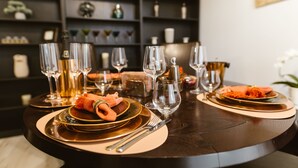 Una mesa de comedor dispuesta con platos, vasos y cubiertos, con una mesa de madera oscura y una estantería al fondo.