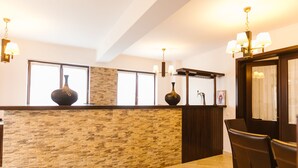 Un área de recepción con pared de piedra, dos jarrones grandes, una araña y una zona de estar con sillas.