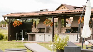 Un área de cocina al aire libre con horno de ladrillo, armarios blancos y flores naranjas colgantes.