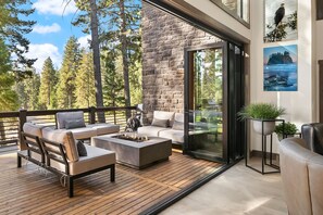 A modern outdoor living space with a stone wall, a glass door leading to a deck, and a view of a forest. - Stunning 6BR Home in Suncadia! Expertly furnished w/Game Rm*Hot Tub*Fire Pit (Cle Elum)