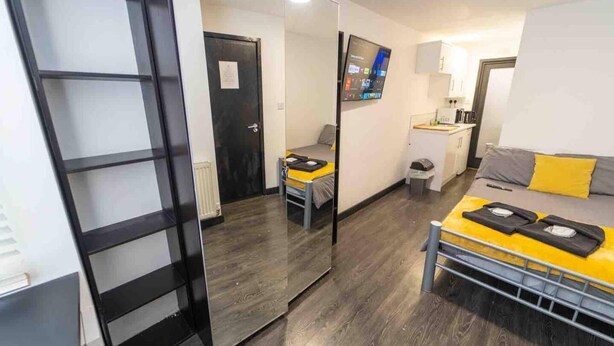 A compact room with a bed, a small desk, a mirror, and a door leading to another room. - Cosy Ensuite Style Studio Close to University! (Birmingham)