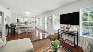 A modern living room with a flat-screen TV, a dining area, and a kitchen.