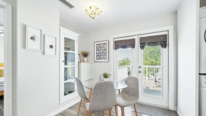 A dining area with a glass table and grey chairs, a white cabinet with glass doors, and a view of the outdoors through a sliding door.