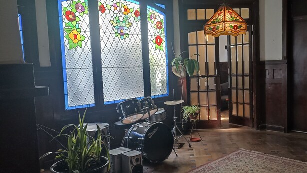 A room with a drum set, a stained glass window, a hanging light fixture, and a wooden door.