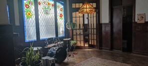 A room with a drum set, a stained glass window, a hanging light fixture, and a wooden door.