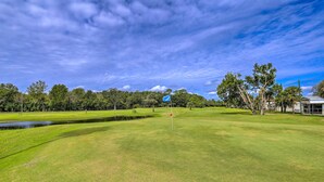 A golf course with a pond, trees, and a blue flag on a flagpole. - 'The Shell House' in Titusville: Pool, Golf Access (Titusville)