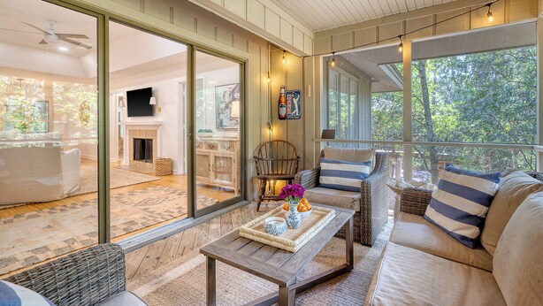 A cozy living room with a sofa, a coffee table with decorative items, and a view of a fireplace and dining area through large glass doors. - Stunning renovated cottage in Inlet Cove (Kiawah Island)