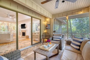 Un salon chaleureux avec un canapé, une table basse agrémentée d’objets décoratifs, et une vue sur une cheminée et un coin repas, le tout visible à travers de grandes portes vitrées.