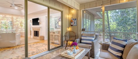 A cozy living room with a sofa, a coffee table with decorative items, and a view of a fireplace and dining area through large glass doors.