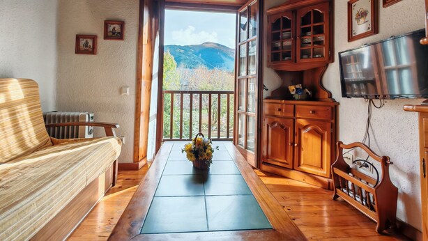 A cozy room with a wooden bench, a radiator, a wooden cabinet, a television, and a view of mountains through an open door. - Spacious apartment with garden Cosmos 1 (Pla de l'Ermita)