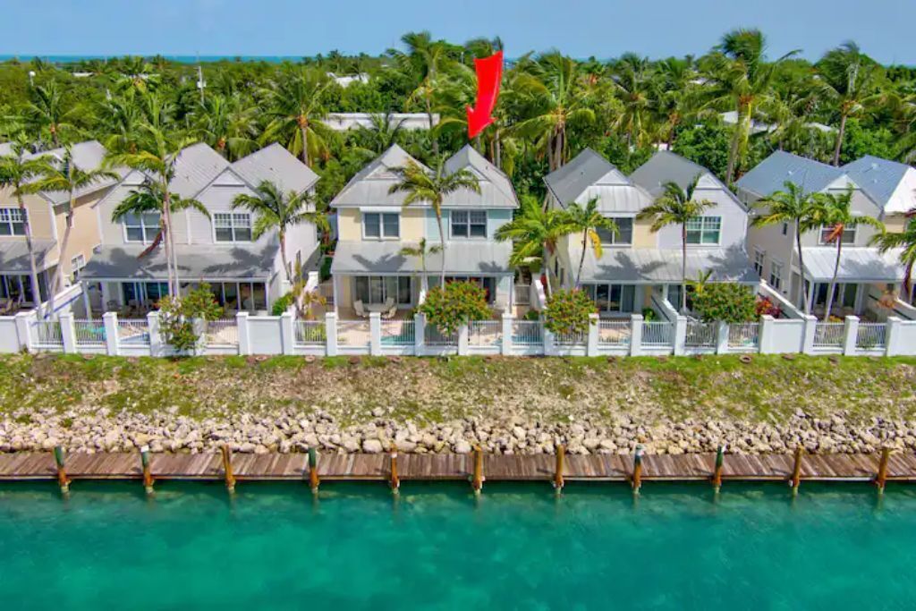A row of beachfront villas with a wooden dock leading to a clear turquoise pool.