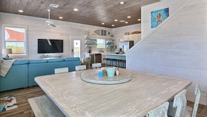 A modern kitchen with wooden cabinets, a dining table, and a blue sofa. - The Beach Buoy by Silver Sands Vacation Rentals (Port Aransas)