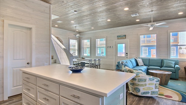 A spacious living area with a large white island, a blue sofa, and a wooden dining table. - The Beach Buoy by Silver Sands Vacation Rentals (Port Aransas)