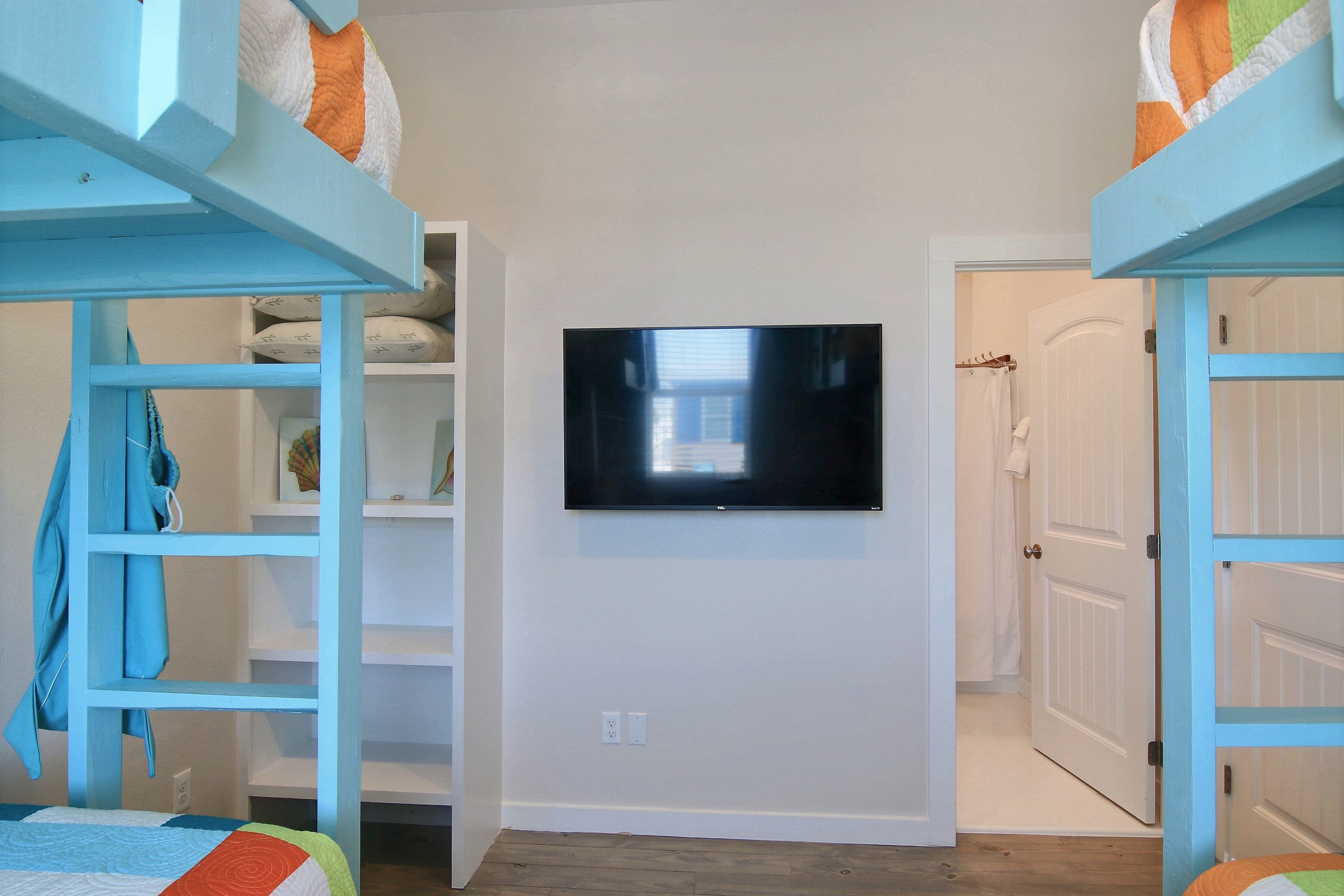 Una habitación con literas, un televisor montado en la pared y una puerta que da a otra habitación.