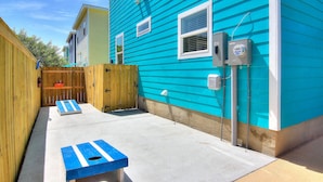A backyard with a wooden fence, a concrete patio, and a blue house. - The Beach Buoy by Silver Sands Vacation Rentals (Port Aransas)