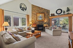 A cozy living room with two sofas, a coffee table, a fireplace, and a large window with curtains. - Charming 2BR Condo in the Heart of Breckenridge! (Breckenridge)