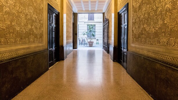 A hallway with ornate wall patterns, a tiled floor, and a view of bicycles and a potted plant in the background. - JOIVY Lovely Flat For 5 Close To Sforzesco Castle (Milan)