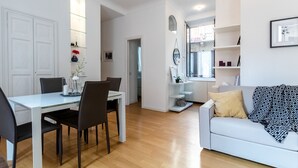 A modern living room with a white sofa, a dining table with chairs, and a kitchen area in the background. - JOIVY Lovely Flat For 5 Close To Sforzesco Castle (Milan)