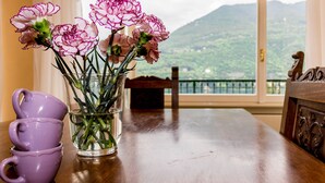 Une table avec un vase de fleurs, une pile de tasses violettes et, par la fenêtre, une vue sur un paysage montagneux.