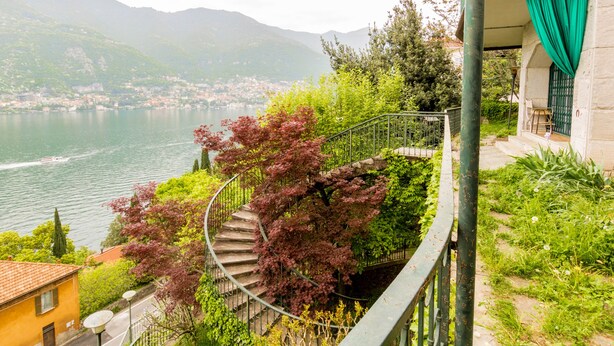Un escalier en colimaçon, entouré d’une végétation luxuriante, qui offre une vue sur un lac et une ville.