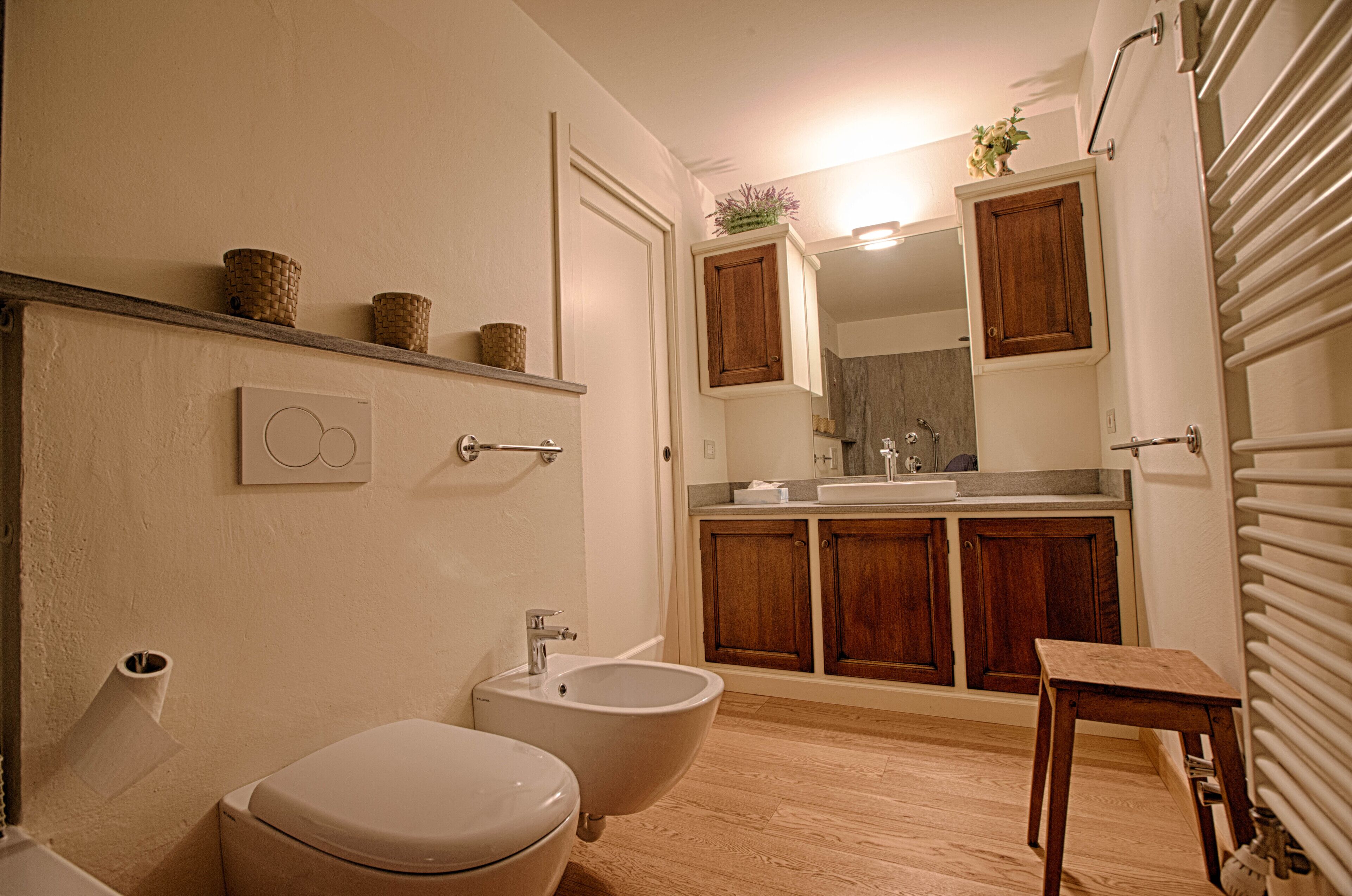 Une salle de bain comprenant des toilettes, un bidet, des meubles en bois, un miroir et un radiateur.
