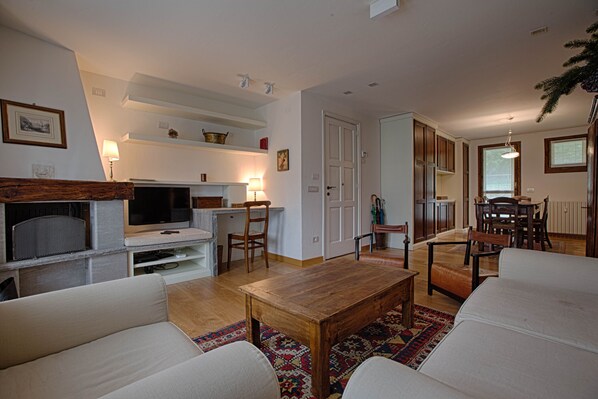 A living room with a TV, sofa, wooden coffee table, and a dining area with chairs and a table. - JOIVY Lovely Apt W/Mountain View And Parking In Courmayeur (Courmayeur)