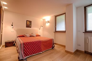 A bedroom with a large bed, two wall-mounted lights, a window, and a wooden nightstand. - JOIVY Lovely Apt W/Mountain View And Parking In Courmayeur (Courmayeur)