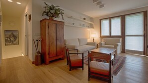 A spacious living room with a wooden floor, a white sofa, a wooden cabinet, and a table with chairs. - JOIVY Lovely Apt W/Mountain View And Parking In Courmayeur (Courmayeur)
