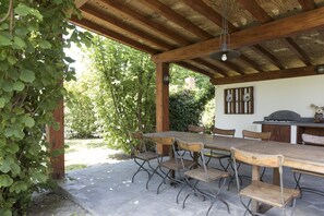 Un patio al aire libre con una mesa y sillas de madera, una lámpara colgante y un suelo de piedra.