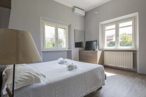 Ett sovrum med en säng, en tv, en lampa och två fönster.