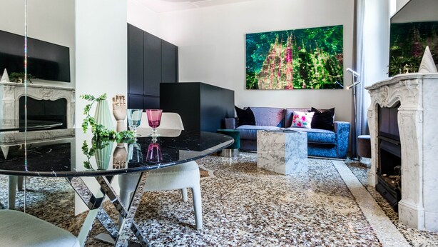 A modern living room with a glass dining table, a sofa, a fireplace, and a large painting on the wall. - JOIVY Superb 1Bed Apt In Brera (Milan)