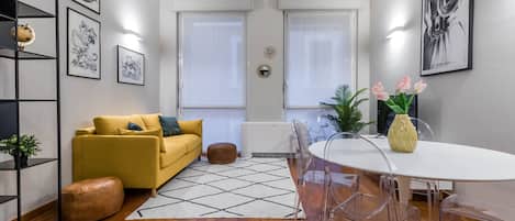 Un salon moderne avec un canapé jaune, une table ronde et un coin repas dont le plateau est en verre transparent.