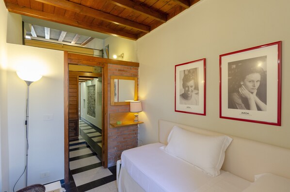 A hotel room with a bed, a nightstand with a lamp, a brick wall, and two framed photographs on the wall.